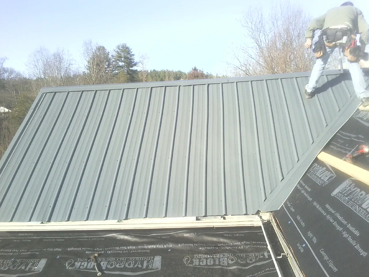 Crew installing dark green standing seam panels over synthetic underlayment in Huntington